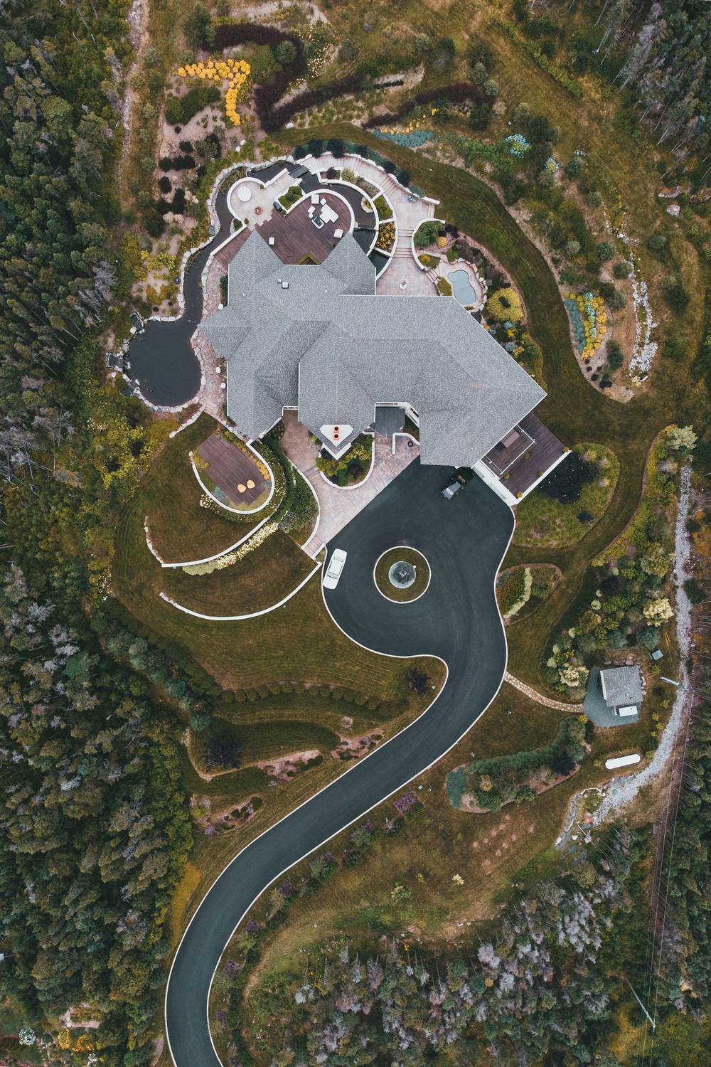 Aerial view of a long, winding black driveway curving through green landscaping